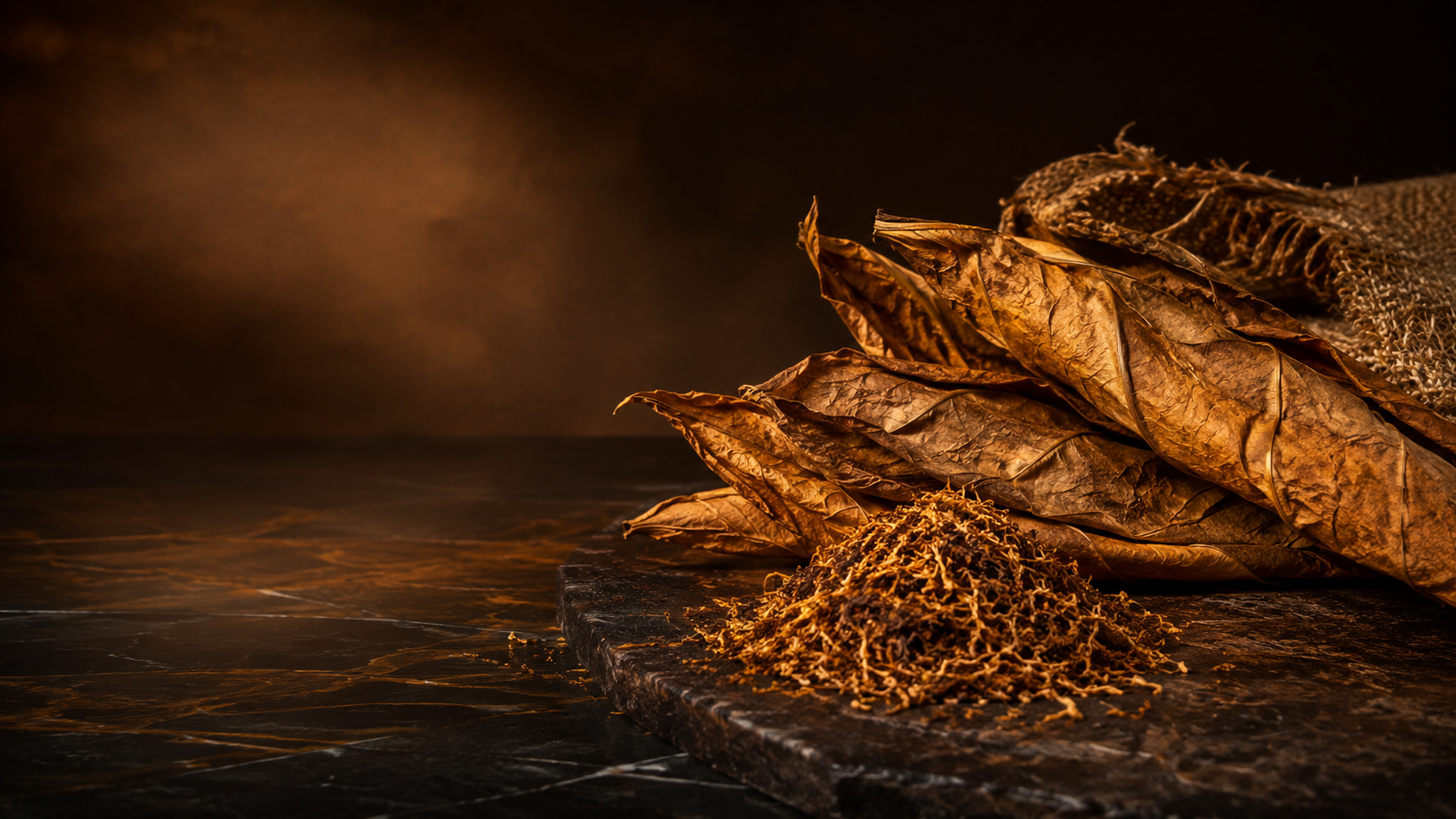 Cured tobacco leaves and loose tobacco on a dark work surface